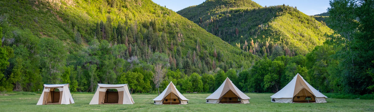 Row of canvas tents and bell-style wall tents set up in a green mountain valley.